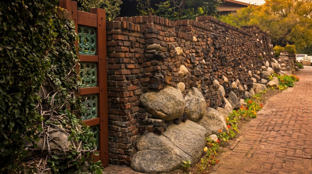 Detail of the boulder-and-clinker-brick wall with a wood-framed panel of green glazed openwork tiles at left, river boulders along the base and a brick walkway to the right.