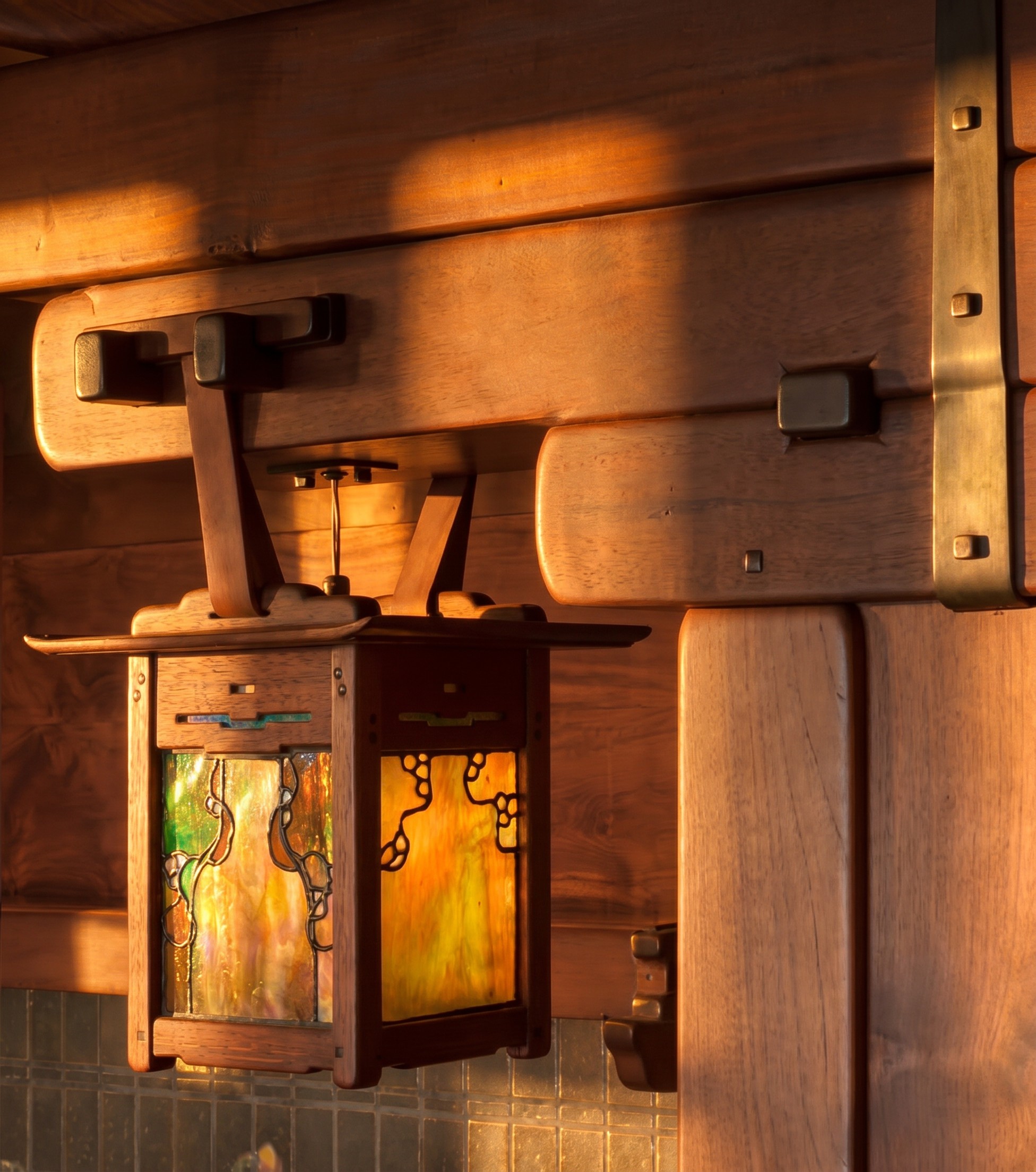 Detail of the leather-strapped art-glass lantern hanging within the Gamble House living-room inglenook, casting warm light over the brick and tile of the fireplace recess