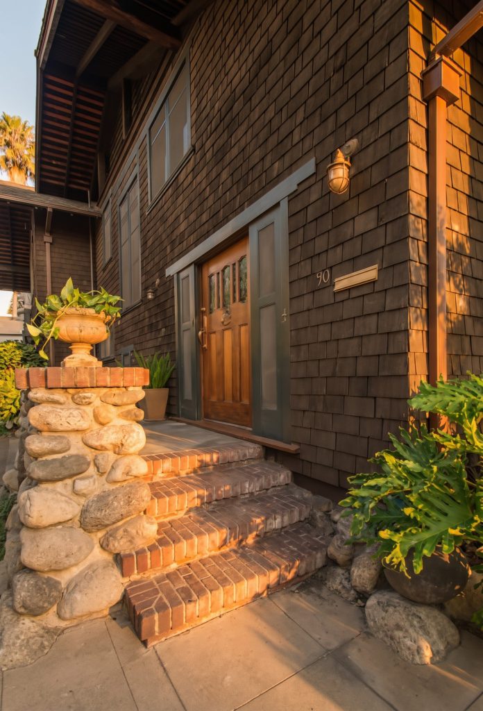 Brick steps and walkway leading up to the covered front terrace and wooden front door of the Louise T. Halsted House, framed by shingled walls under a deep eave