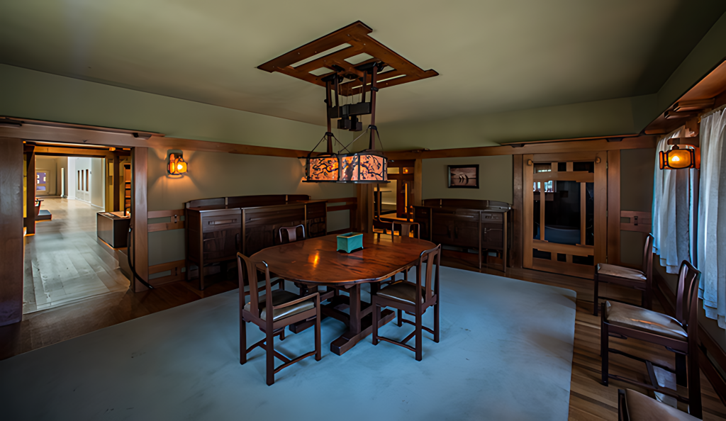 Dimly lit view of the recreated Robinson dining room at the Huntington, the leaded-glass ceiling fixture and two wall sconces glowing, original sideboards along the walls beneath a green ceiling, and an open doorway at left leading into a bright museum gallery.
