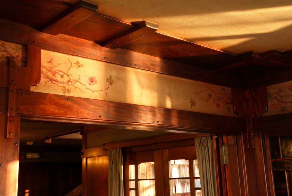 The upper wall of the Thorsen House living room, where a hand-painted frieze of climbing roses runs above the oak paneling and below the ceiling beams.