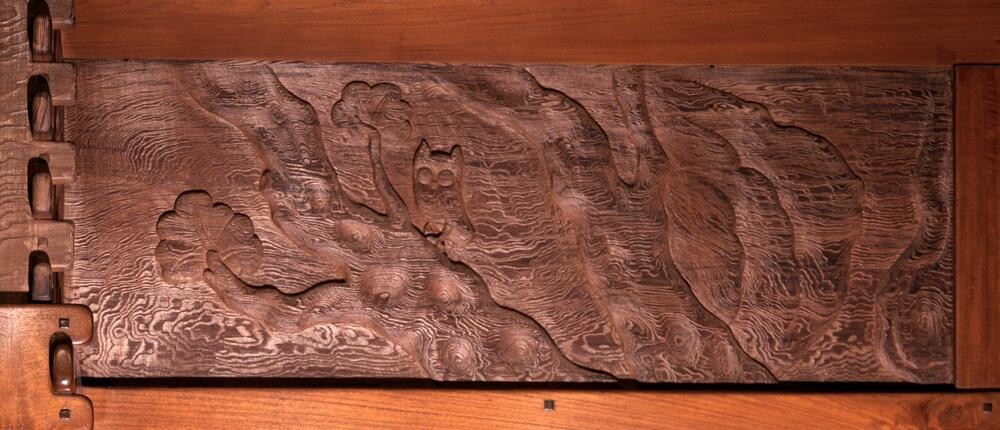 Carved redwood frieze panel at the Gamble House depicting an owl perched in a gnarled tree, the wood grain swirling around the shallow relief