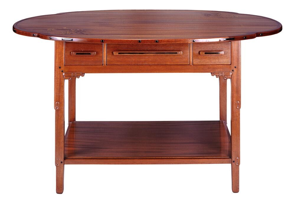 A Greene & Greene library table in mahogany: a long top with rounded ends and a delicate inlaid floral sprig, three drawers with recessed pulls across the apron, small carved brackets at the leg tops, square legs, and a full lower shelf.