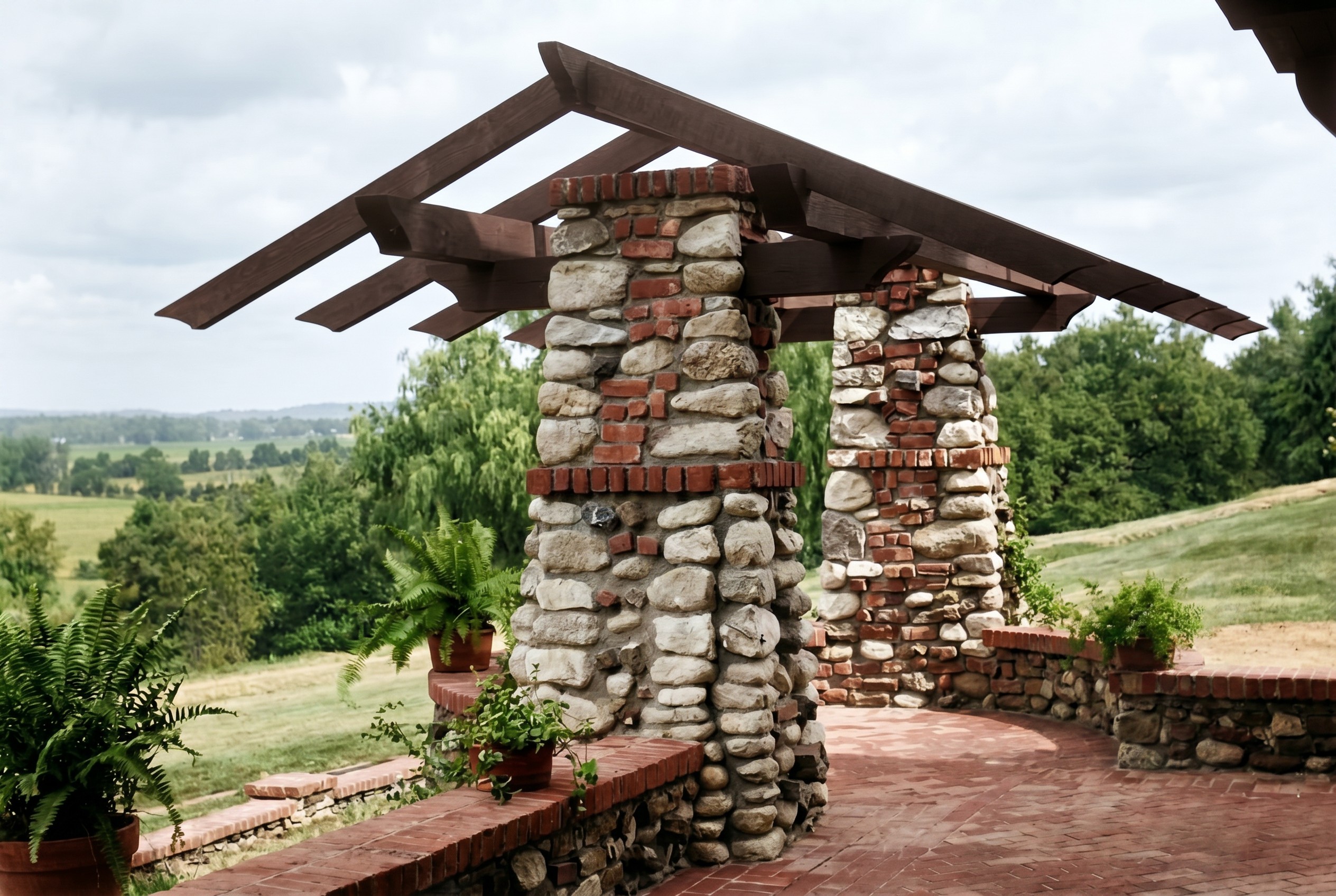 A detail of the rear pergola at the James Culbertson House: two piers of river boulder and brick supporting cantilevered timber beams above a brick terrace, open country beyond.